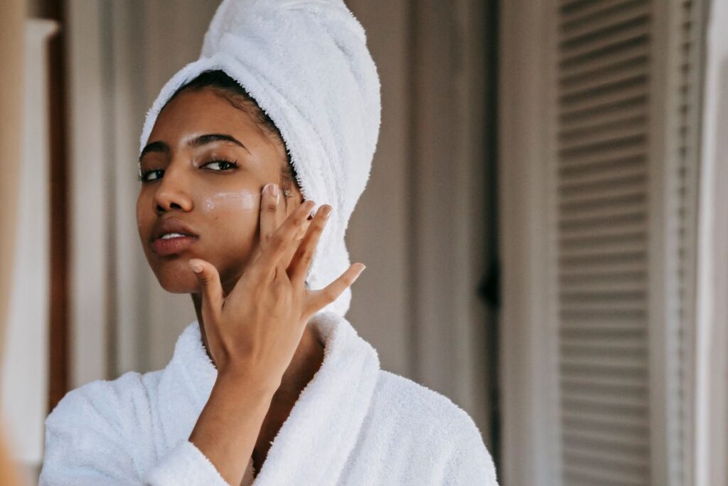 Femme qui hésite à appliquer une crème riche sur le visage devant le miroir